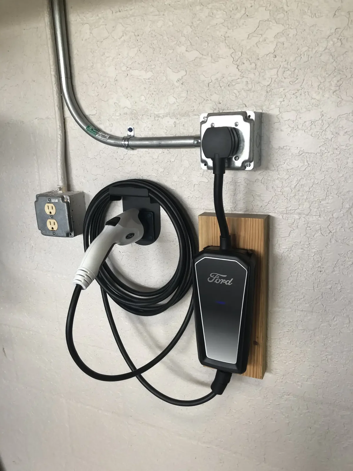 Ford portable EV charger plugged into a wall-mounted NEMA 14-50 outlet with metal conduit.